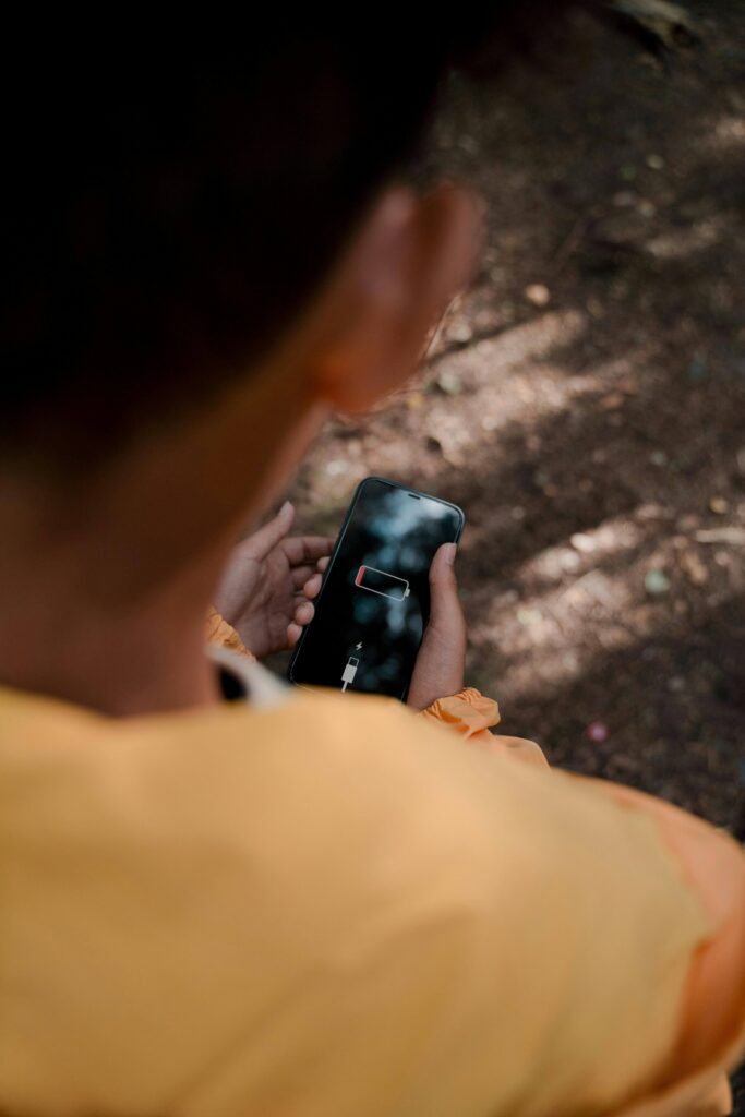 Camper in a yellow jacket holding a smartphone with a low battery warning, searching for power solutions for devices while camping in the wilderness